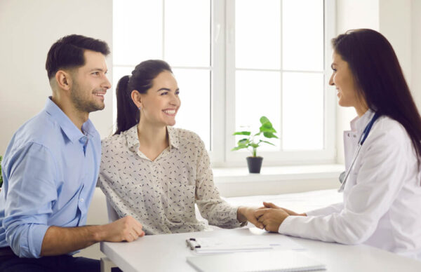 A smiling couple discussing surrogacy with a fertility specialist